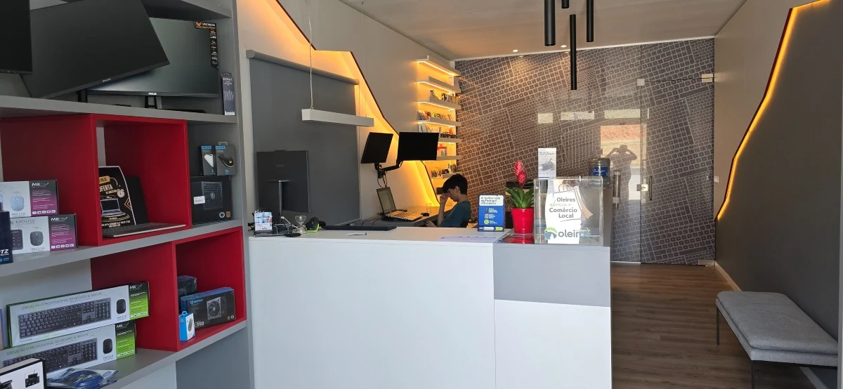 Interior da InforAlvelos: parede cinzenta com luz âmbar em diagonal, nichos vermelhos e balcão claro